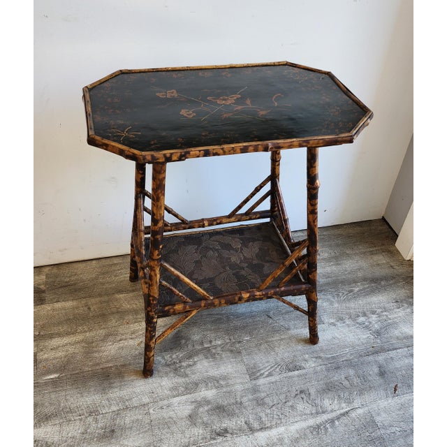 The table features a distinctive octagonal top finished in a rich, black Japanned lacquer. The surface is hand-painted...