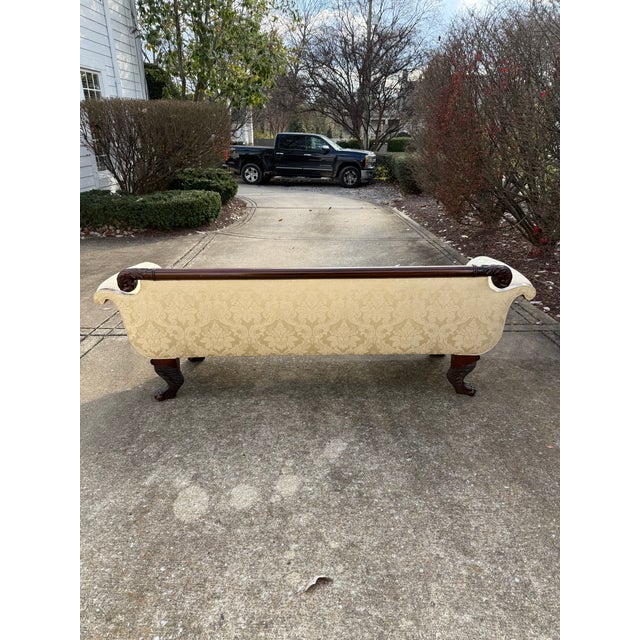 Vintage American Empire sofa covered in cream silk damask fabric. Sofa features rolled arms, elaborate carved details and...