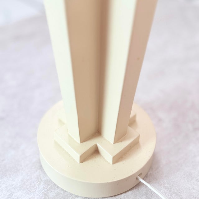 A bold postmodern table lamp in a soft cream finish, built around an architectural column form with a dramatic sphere...