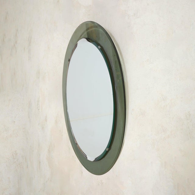 An Italian wall mirror from the 1960s, attributed to Max Ingrand for Fontana Arte. The oval silhouette is simple and...