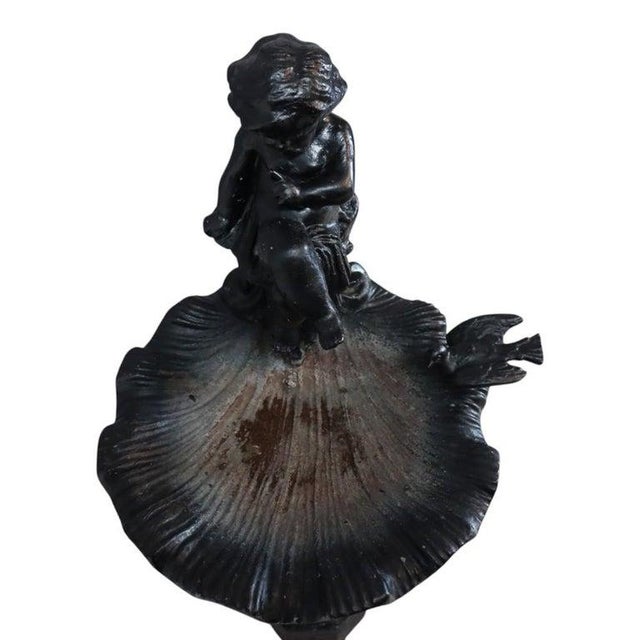 An antique cast iron birdbath, dating to approximately 1920, featuring a figural cherub and seashell motif. A charming...
