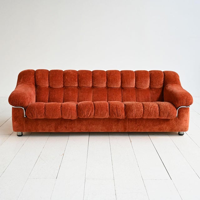 Upholstered three-seater sofa with rust-colored velvet upholstery, featuring quilted workmanship and tubular steel...