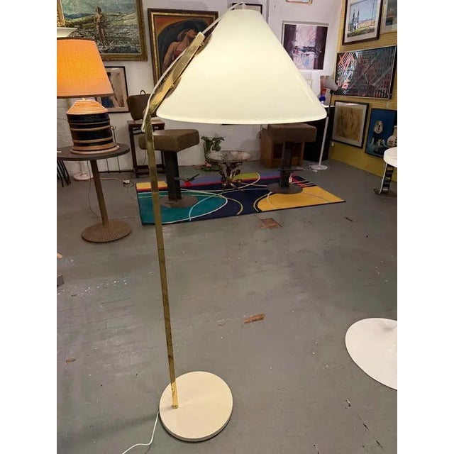 This elegant floor lamp features a slender brass stem rising from a round lacquered brass base. The adjustable arm...