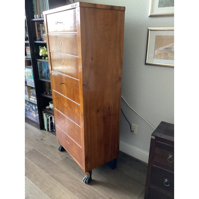Exemplifying the understated elegance and functional sophistication of the period, this antique Biedermeier tall chest of...