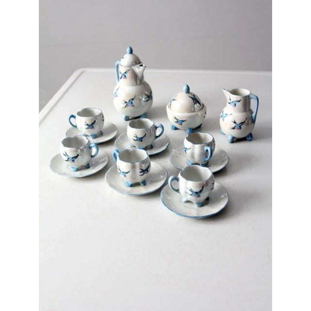 This sweet miniature tea set is early 20th century German. Pretty blue birds fly across the iridescent white dishes with...