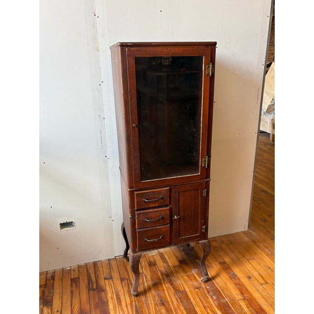 A classic, upright medical-style cabinet designed for utility and display. Features a single glass door for showcasing...