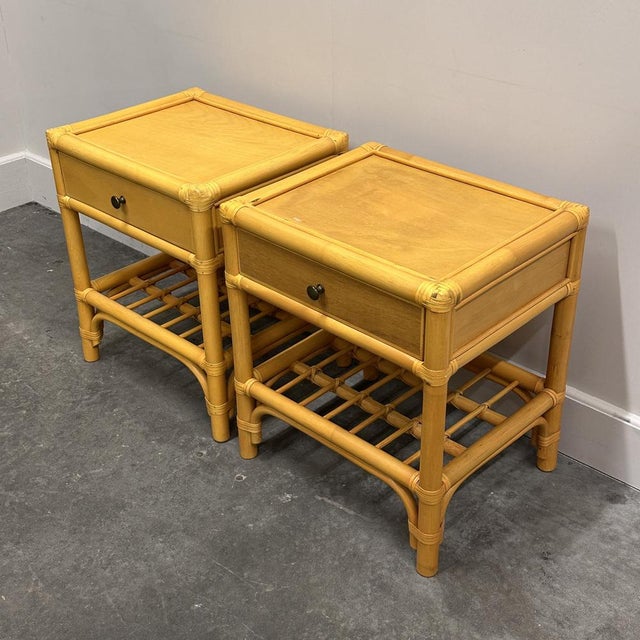 A charming pair of vintage 1970s bamboo and wood nightstands, featuring warm honey tones, a single drawer for storage, and...