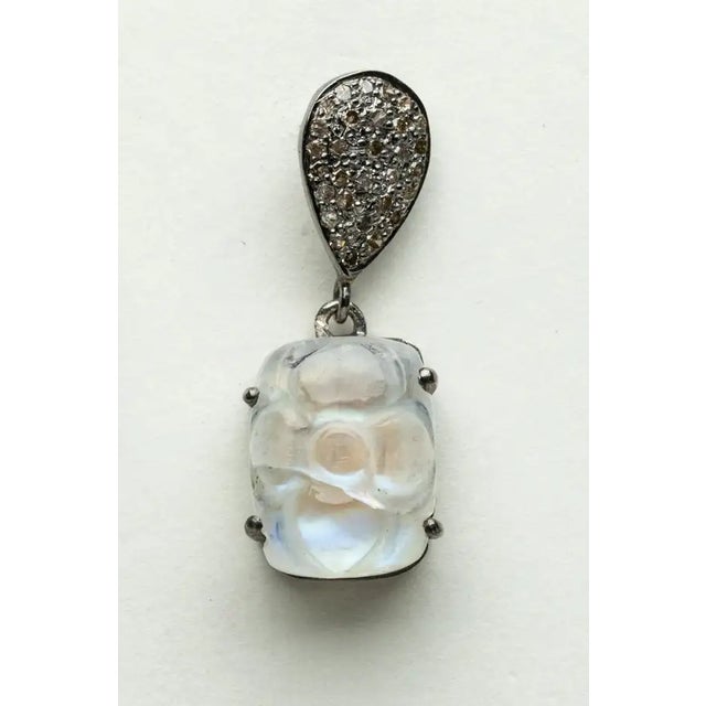 A pair of rainbow moonstone drop earrings featuring a carved floral design on the top of the rectangular cabochon...