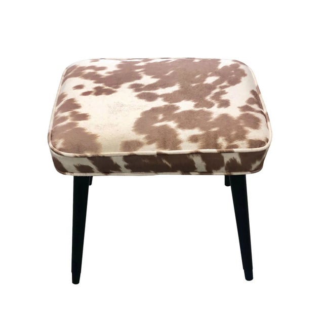 A rectangular mid century stool. Black lacquered wooden legs with gold tips. Upholstered in cowhide suede. Circa 1950s.