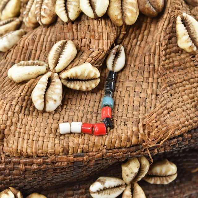 The frame of this cap is made of vegetal fibers using basketry techniques. It is intricately embroidered with cowry...