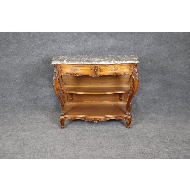 This French carved walnut two-tier open buffet console table is an exquisite example of fine craftsmanship and timeless...