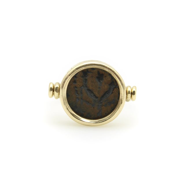 Encased in a circular 14k gold bezel is an ancient bronze coin. On one side of the coin, there is a plantlike image; on...