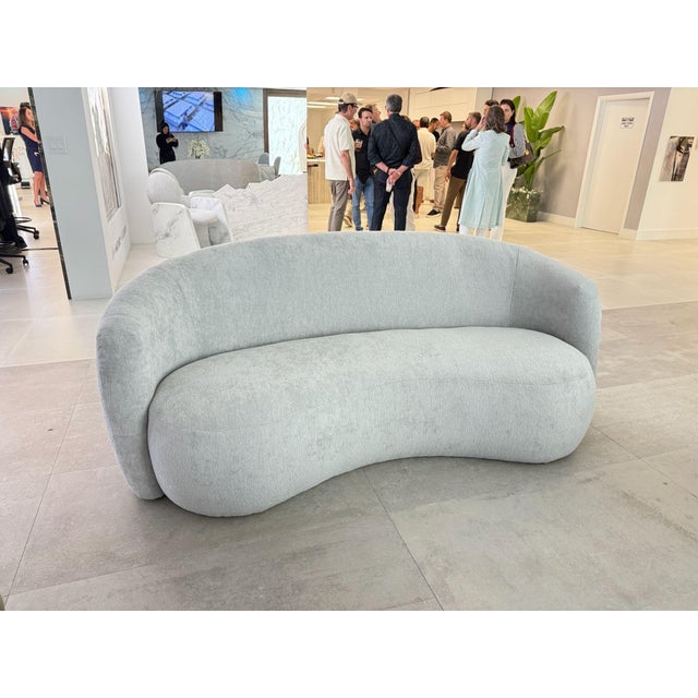 Modern curved sofa upholstered in a soft neutral fabric, featuring a sculptural silhouette and generous proportions....