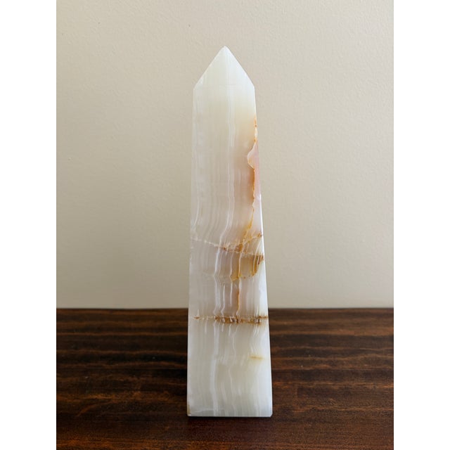 A beautifully proportioned onyx marble obelisk in richly veined shades of green, cream, and brown. The sculptural...