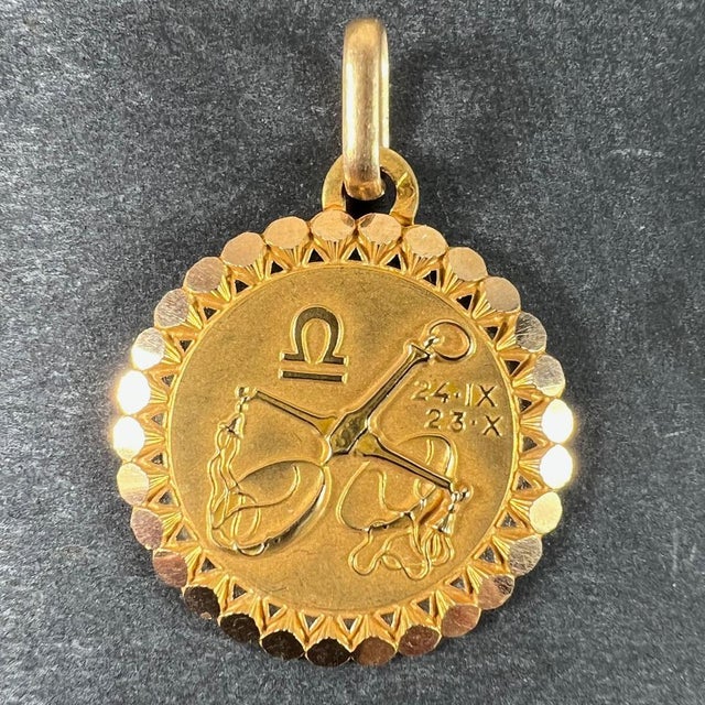 An 18 karat (18K) yellow gold charm pendant designed as the Zodiac sign of Libra, depicting a pair of scales with the...