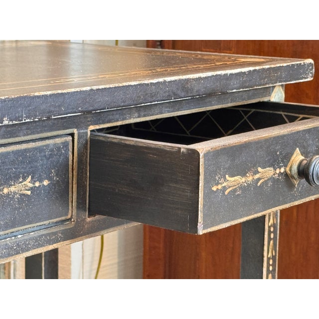Black painted table with three drawers, decorated throughout with painted borders and small floral motifs — on the top,...