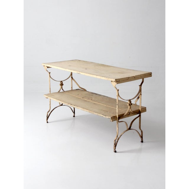 An antique French garden table featuring a two-tier design and a painted iron base with delicate scrollwork. The plank...