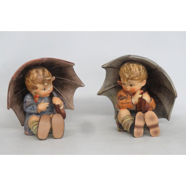 This adorable Figurine Pair is made of porcelain finished ceramic. This charming Hummel pair are titled "Girl with...