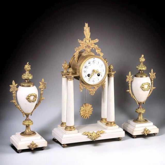 A refined French mantel clock garniture set, dating to the 19th century, executed in gilt bronze and white stone. The...