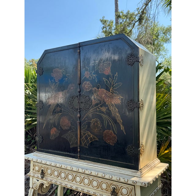 An exquisite 1920s Chinoiserie-style cabinet featuring a richly decorated black lacquer finish with hand-painted gilt...