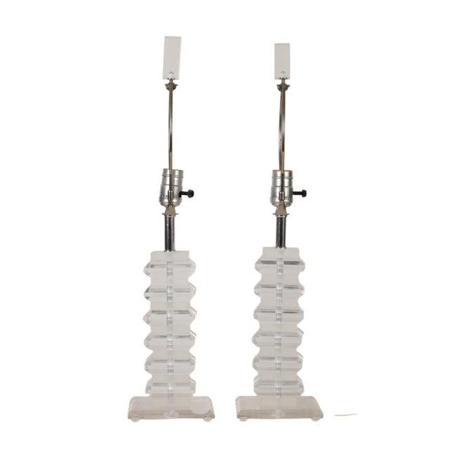 A pair of 1970's modern geometric clear Lucite table lamps. The Lucite is stacked to enhance its 1970's look. Each lamp...