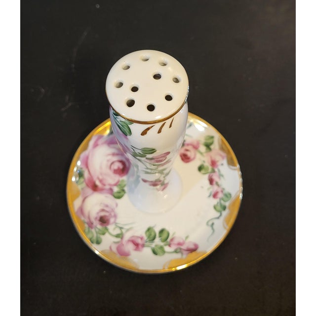 Elegant porcelain hatpin holder with a delicate floral design and gold accents. A functional and decorative piece for...