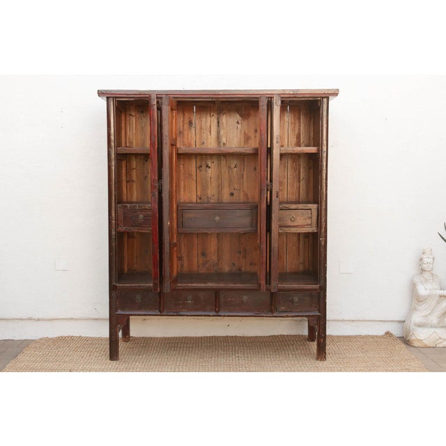 Four paneled doors open to reveal a run of shelves and three interior drawers, framed in a dark lacquer finish accented...