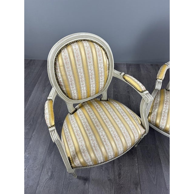 An elegant pair of Louis XVI style medallion armchairs with a matching footstool. The armchairs rest on fluted, tapered...