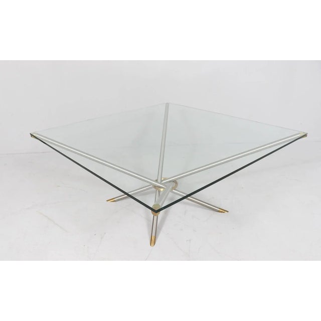 solid construction made of aluminum and brass, with a square glass top This piece is attributed to the mentioned...
