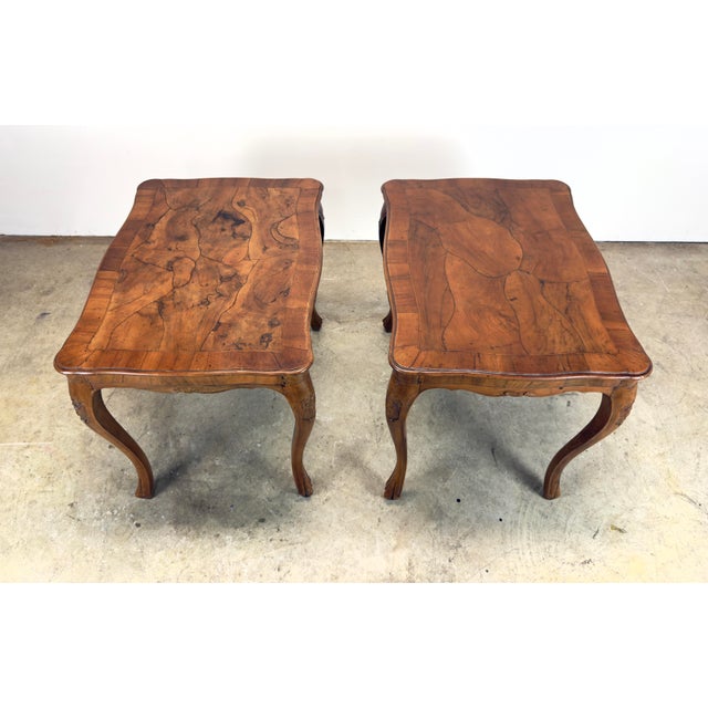 A pair of Italian rococo style tables featuring a patterned olive or walnut burl wood top, a band of satinwood along the...