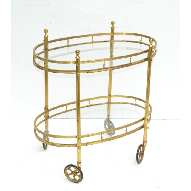 Superb bar cart made by Maison Bagués in France circa 1950. Features 2 tier glass shelves with brass detail in oval shape....