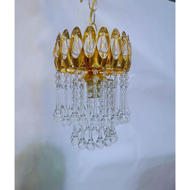 This ornate gold‑tone chandelier features a sculpted metal crown accented with elongated teardrop crystals and layered...
