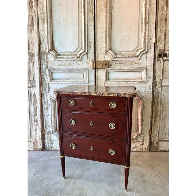 A small louis xvi style mahogany commode, dating from the mid-20th century. The front features three drawers, each with a...