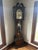 Traditional tall-case clock with swan-neck pediment, classical columns, ornate dial, three weights and a pendulum visible...