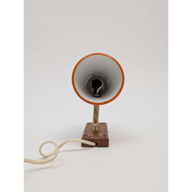 Vintage 1960's metal cone wall sconce has a dark orange paint exterior with bright white interior and a teak wood base.