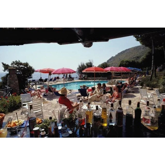 Poolside Bar 1980 by Slim Aarons Slim Aarons Limited Estate Edition Guests seen from a poolside bar at the Hotel Il...