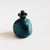 A small vintage studio pottery perfume bottle. Triangular shape with a dark teal glaze. A matching dauber is glazed at...