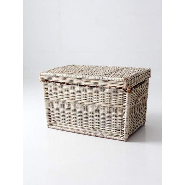 This vintage white painted wicker storage basket features a hinged lid and woven side handles, crafted in a classic...