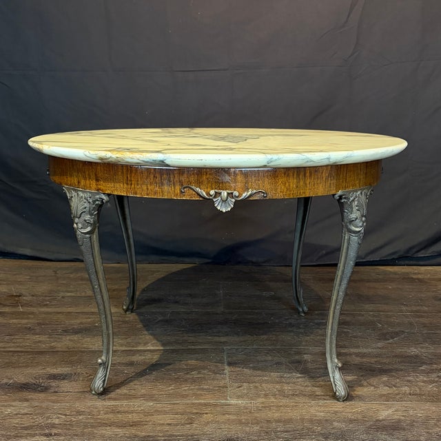 Elegant French coffee table with a beautifully veined marble top resting above a richly toned frieze, centered by a...