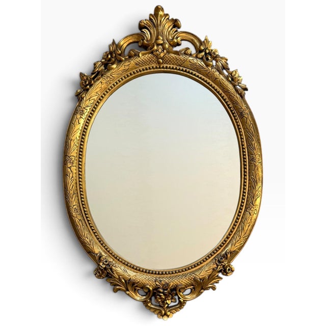 A spectacular vintage Italian oval wall mirror by Euromarchi S.r.L., featuring an elaborately sculpted gilt-gold frame...