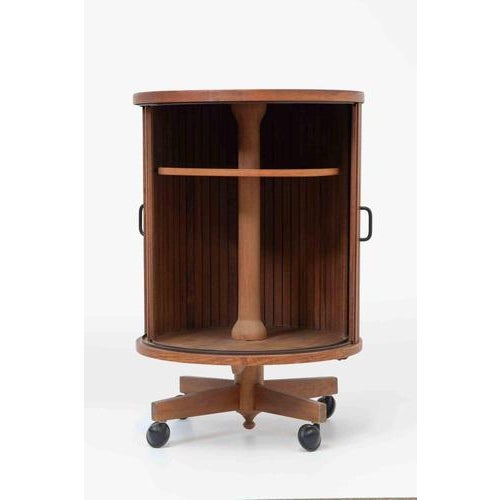 A sculptural cylindrical bar cart or storage cabinet in warm-toned wood, representative of mid-century Italian modern...