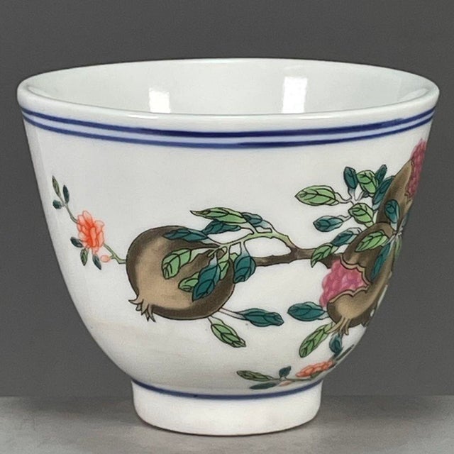A charming Chinese porcelain tea cup. The exterior is finely hand-painted in vibrant Famille Rose enamels, featuring a...