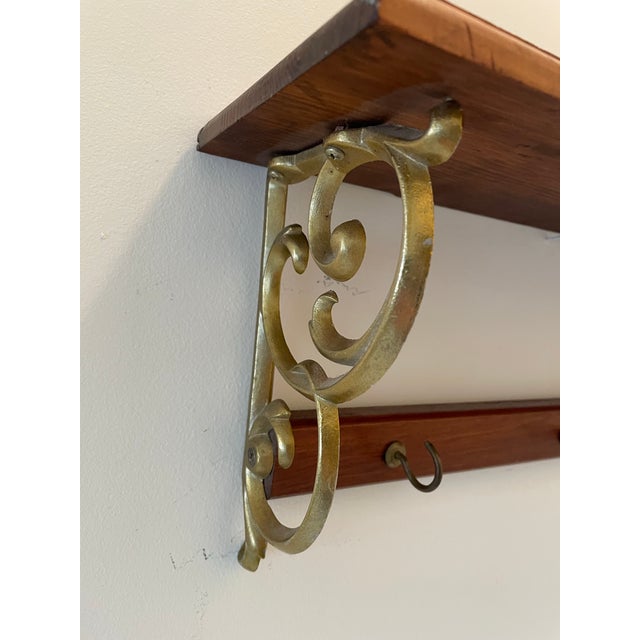 Vintage 1970s wall-mounted shelf featuring substantial cast metal scroll brackets in a warm aged brass-tone finish and...