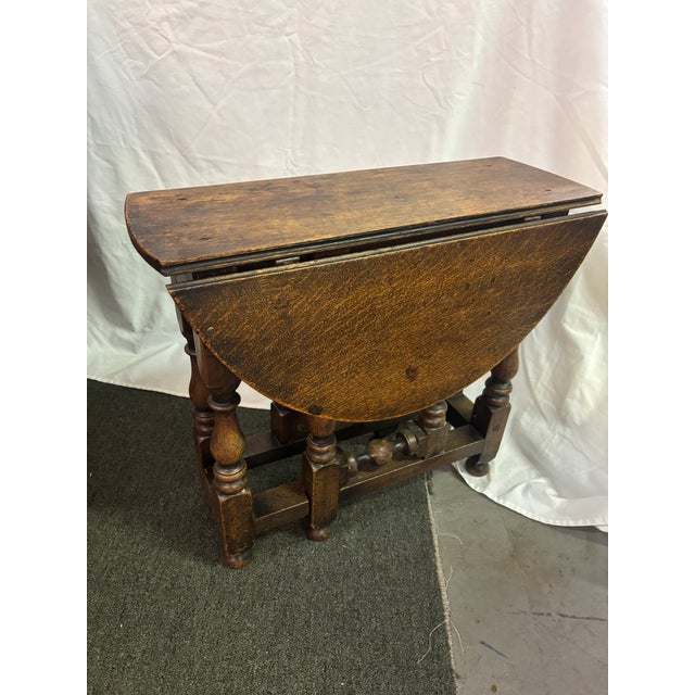 A diminutive Jacobean style Oak Gateleg Table, late 19th century, with a round top over crisply-turned supports ending in...