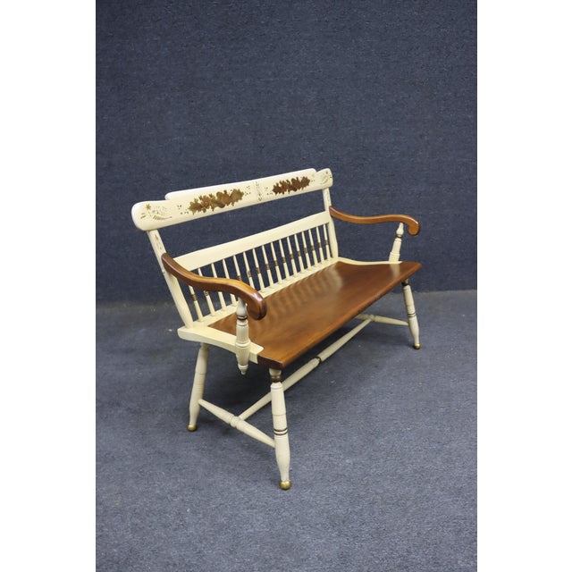 Hitchcock-style maple bench featuring a cream-painted frame, warm wood seat, and curved arms with contrasting wood...