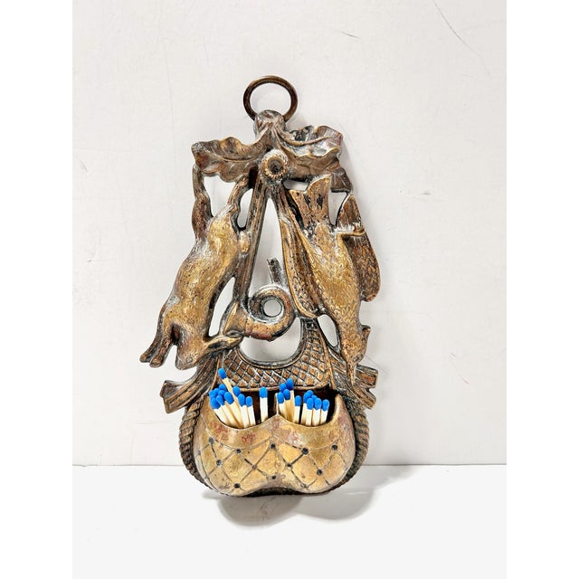 A striking antique brass wall match safe and striker featuring detailed figural relief of a rabbit and bird or pheasant...