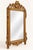 An ornate gilded mirror crowned by a sculptural violin-and-foliage crest. Carved ornament continues along the frame and...