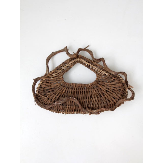 A vintage woven wall basket crafted from natural vine around a sculptural branch frame, with an open top and irregular...