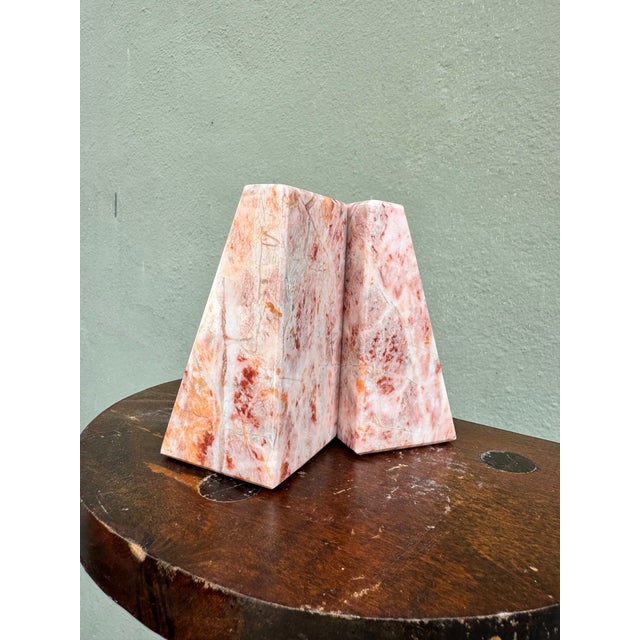 A sculptural pair of solid pink marble bookends in a clean wedge form, hewn from richly veined rose marble with sweeping...
