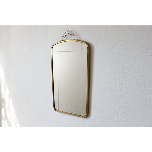 A wall mirror with a rectangular shape that tapers slightly toward the bottom, set within a slender brass frame with...